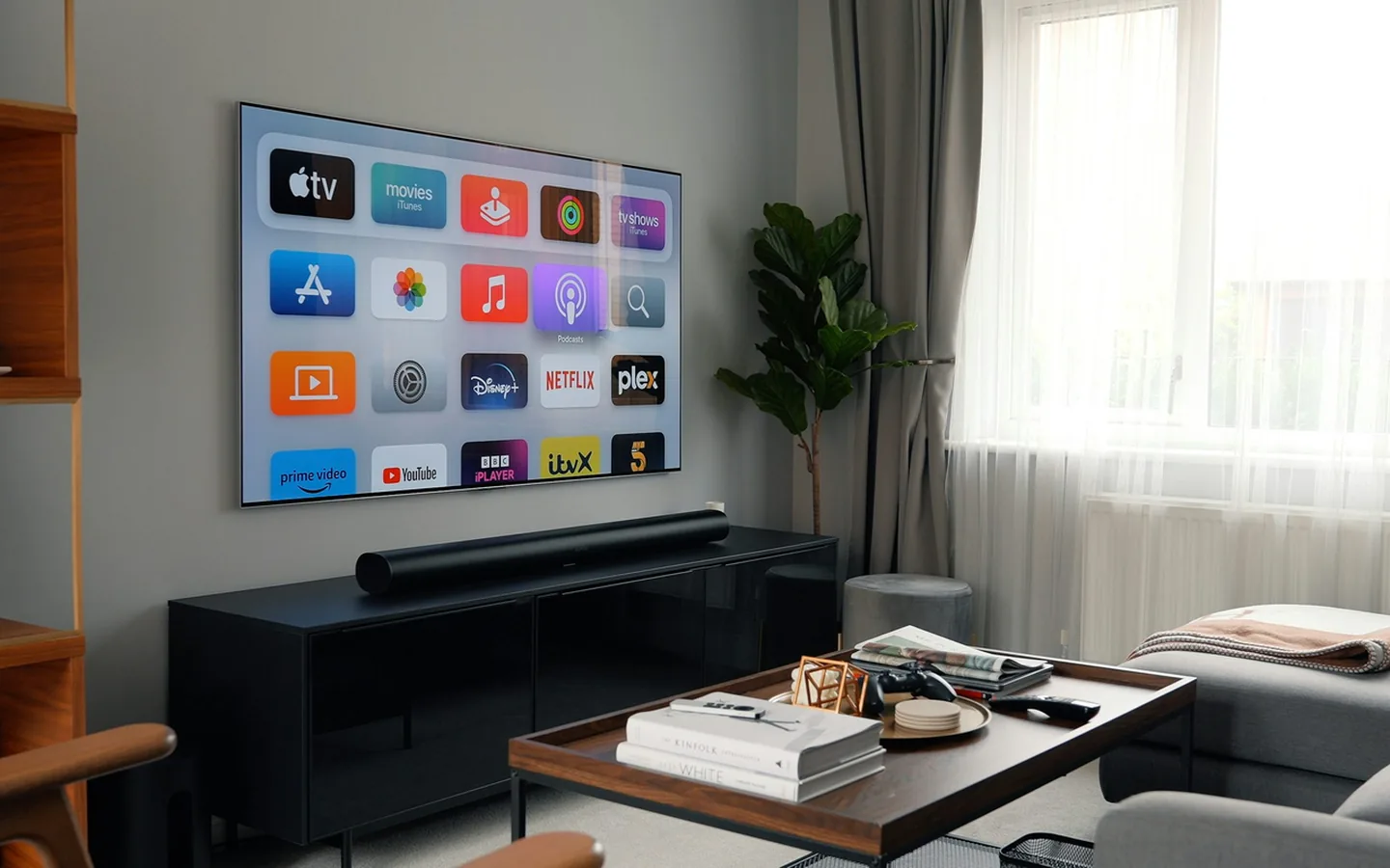 O guia de programação funciona como uma grade impressa dentro do aplicativo. Televisor na parede exibindo uma grade de aplicativos organizada em blocos, com soundbar e mesa de centro abaixo