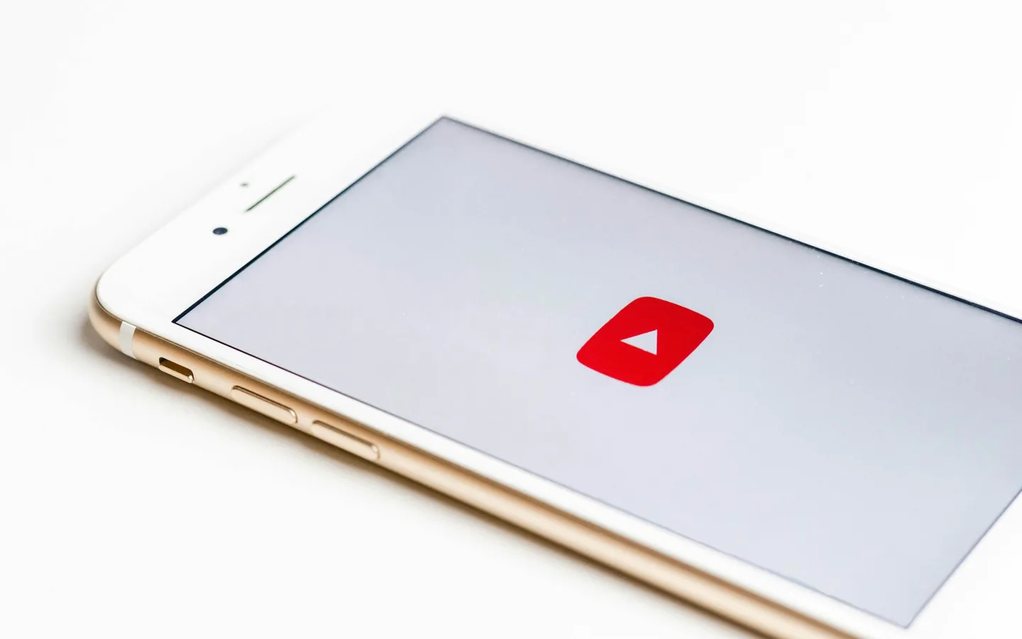 A loja de onde o aplicativo vem diz muito sobre o risco que você assume. Celular branco e dourado apoiado sobre superfície clara exibindo um ícone de play vermelho na tela