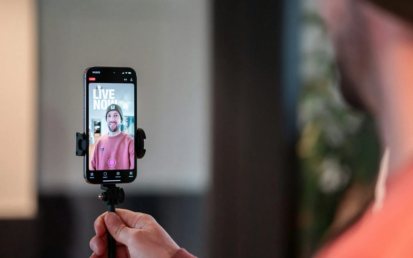 No celular, o mesmo acesso funciona dentro e fora de casa. Celular preso a um tripé transmitindo ao vivo, com a imagem de uma pessoa na tela e um selo indicando transmissão em andamento