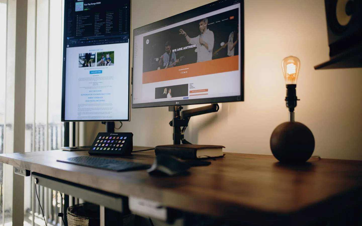 Renovação, cancelamento e limite de telas moram nos termos, não na propaganda. Mesa de escritório com dois monitores exibindo páginas na web, teclado, controlador de teclas e luminária acesa
