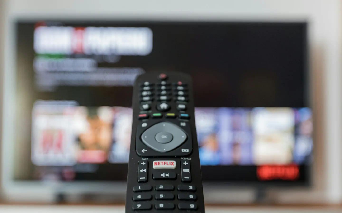 Um teste bem conduzido responde perguntas objetivas, não impressões. Controle remoto preto em primeiro plano diante de um televisor desfocado exibindo um catálogo de títulos