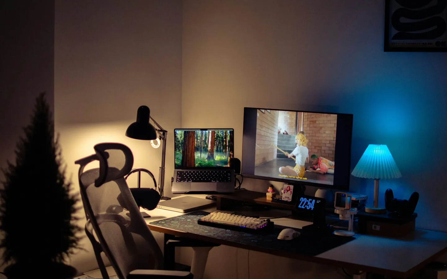 Legendas e áudio alternativo dependem de o conteúdo trazer essas faixas. Monitor exibindo um vídeo com legendas na tela, ao lado de notebook aberto, teclado e iluminação colorida ao fundo
